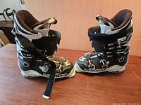 Side view of black and white Salomon ski boots with four buckles and Velcro straps on wooden surface.