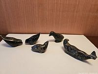 Five soap stone carvings including seal, walrus, and three birds on white background with brown wall