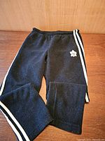 Full view of folded black fleece pants with white stripes on the sides, showing elastic waistband and overall condition.