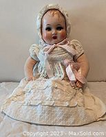Full view of the vintage composite baby doll seated, showing original cream lace dress and bonnet with pink ribbon