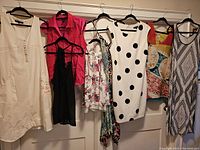 Seven women's clothing pieces hanging on hangers on a door, showing the variety of colors and prints included in the lot.