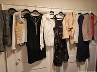 View of 8 women's garments hanging on a rod including dresses, jackets, and tops in neutral colors