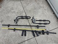 Full view of car rails, kayak holders, and keys laid on pavement with measuring tape showing length.