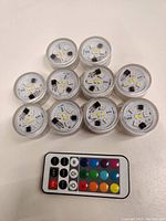 Top-view of 10 submersible LED tea light candles arranged with remote control in front, showing electronic components inside translucent casing.