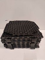 Stacked view of black rubber interlocking floor tiles showing the grid pattern on surface and tab connectors on sides.