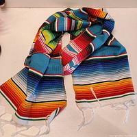 Brightly colored striped scarf laid out and folded showing vivid blue, red, yellow, green and other stripes with white fringed ends.