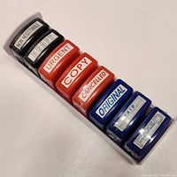 Photo of 8 self-inking stamps in a row with labels NON NEGOTIABLE, DRAFT, URGENT, COPY, CANCELLED, ORIGINAL, PAID, FIXED.