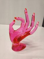 Front and side views of the pink translucent acrylic hand-shaped jewelry display with red-tinted fingertips and a stable base.