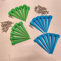 Top-down view of green and blue watering cones with their corresponding small gray drip attachments arranged nearby on a light surface.