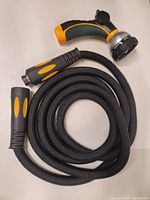 Coiled flexible garden hose with both ends showing soft grip handles, one end has spray nozzle handle.