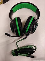 Front view of black and green gaming headset with microphone and coiled cable with inline control.
