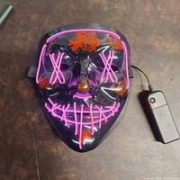 Photo of the LED purge mask on a brown surface, showing the pink lit design and red splatter accents
