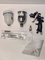 Top view of HVLP spray gun, two paint cups, wrench set, air fitting, and cup guard laid out on white background.