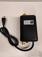 Front view of black mini electric tankless water heater with brass connectors and power cord.