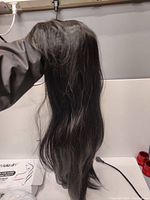 Photo showing long straight synthetic black hair wig held upright, displaying length and texture.