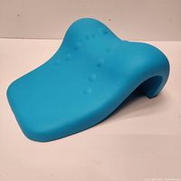 Blue cervical traction device shown at an angled side view highlighting curved ergonomic shape and raised massage nodes.