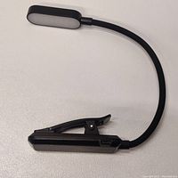 Photo of the clip-on lamp laid flat, showing the closed clip base and flexible neck with elongated oval LED light panel.