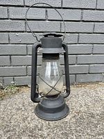 Full view of the black cast metal lantern with clear glass globe and side lift handle.