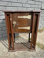 Front view of antique wooden chairside table humidor showing brass hinges and key lock plate on the door, with open lower shelf and vertical supports with geometric cut-outs.