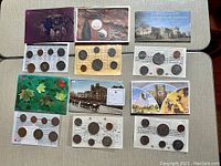 Overview photo showing six Canadian proof-like coin sets arranged on a flat surface with varied colored packaging and protective sleeves containing coins