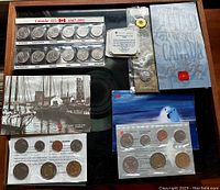 Full photo of all coin sets and collectibles on display on a black surface including Canada 125 quarter set, proof-like sets, V-Day Remembrance bookmark and 1992 commemorative coin.