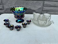 Carnival glass punch bowl set with seven matching iridescent cups and clear Jeannette glass creamer set with sugar, jar, and tray.