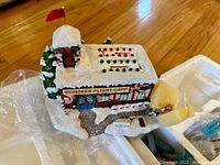 View of decoration showing snowy roof with red and green decorative lights and snow-covered trees beside the building.