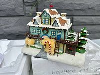 Photo of the Doggie Dormer decorative collectible showing front view with snow-covered roofs, wreaths, candy cane, trees, and fence in a festive Christmas town setting.