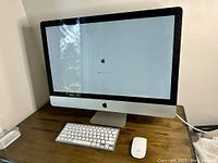 Front view of Apple iMac desktop computer powered on, showing loading screen with Apple logo and wireless keyboard and mouse on desk.
