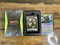 Photo showing box with Magic the Gathering Commander logo, box contains Elf Warrior token cards, with one oversized foil Planeswalker card Freyalise, Llanowar's Fury next to it.