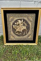 Full front view of framed Burmese Kalaga tapestry showing detailed figure on horseback in silver and gold thread on black velvet background in gold frame with linen mat.