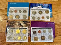 Four sets of Canadian proof like coin sets displayed on wood surface, each with protective packaging and a colorful cover with Royal Canadian Mint branding.