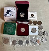 Top view of the entire coin collection showing the 2012 Fine Silver Loonie coin in case with box and certificate, 2003 silver Les Voltigeurs de Quebec nickel in case with green booklet, multiple loose and holder coins including 50 cent pieces and early pennies.
