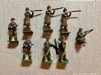 Nine vintage Britains diecast military toy soldier figures arranged standing and kneeling showing different poses and uniforms mostly camouflaged with some brown uniforms and pith helmets
