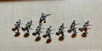 Top view of 10 Britains diecast Confederate toy soldier figurines arranged in a single line on a cream fabric background.