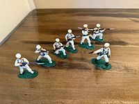 Seven painted metal Navy militia soldier figures on green bases holding rifles with bayonets in a line on trimmed wooden surface
