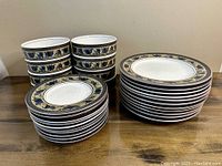 Photo showing stacks of small plates, medium plates, and bowls with Arabella pattern, displaying floral and rope trim design.