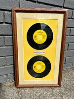 Framed two vintage Rolling Stones 45 rpm vinyl records with yellow background and wooden frame.