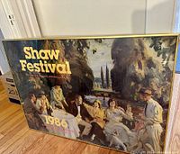Framed poster showing the full artwork with people seated outdoors under trees, displayed on wooden floor.