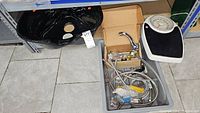 Lot showing black basin, faucet, plumbing components in a plastic container, and a mechanical bathroom scale on the floor.