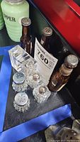Photo showing six various salt and pepper shakers including two beer bottle shaped glass ones, two clear square glass ones, two round faceted glass ones, and a pale green ceramic pepper shaker.