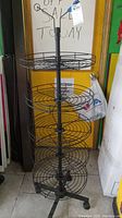 Five tiered metal rolling store display rack with circular wire basket shelves and caster wheels in front of a yellow door.