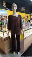 Full height front view of the mannequin, dressed in brown top and black pants.