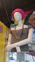 Front view of torso mannequin wearing gray top, pink beret, and multicolored bead necklace.
