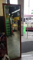 Full length rectangular mirror with brown wooden frame visible, leaning inside a store environment.