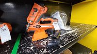 Paslode orange and black power nailer with accessories located on a shelf, including battery and charger.