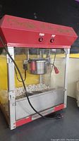 Front view of vintage red popcorn machine with glass sides, filled with popcorn.