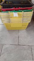 Stacked yellow plastic shopping baskets at bottom with a few black, red and green baskets on top.