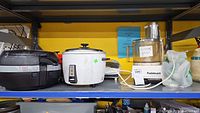 Shelf view showing T-fal Actifry, white rice cooker, Cuisinart food processor, George Foreman grill and other kitchen appliances.