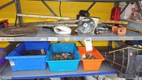 Wide view of metal shelves holding three bins with assorted hardware and tools, plus some items on top shelf including tape measure and metal parts.